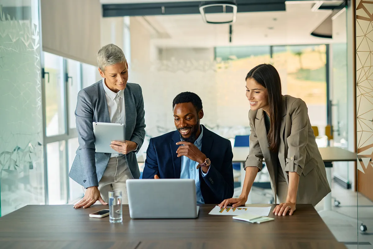 two women leaning over a man who's looking at a laptop