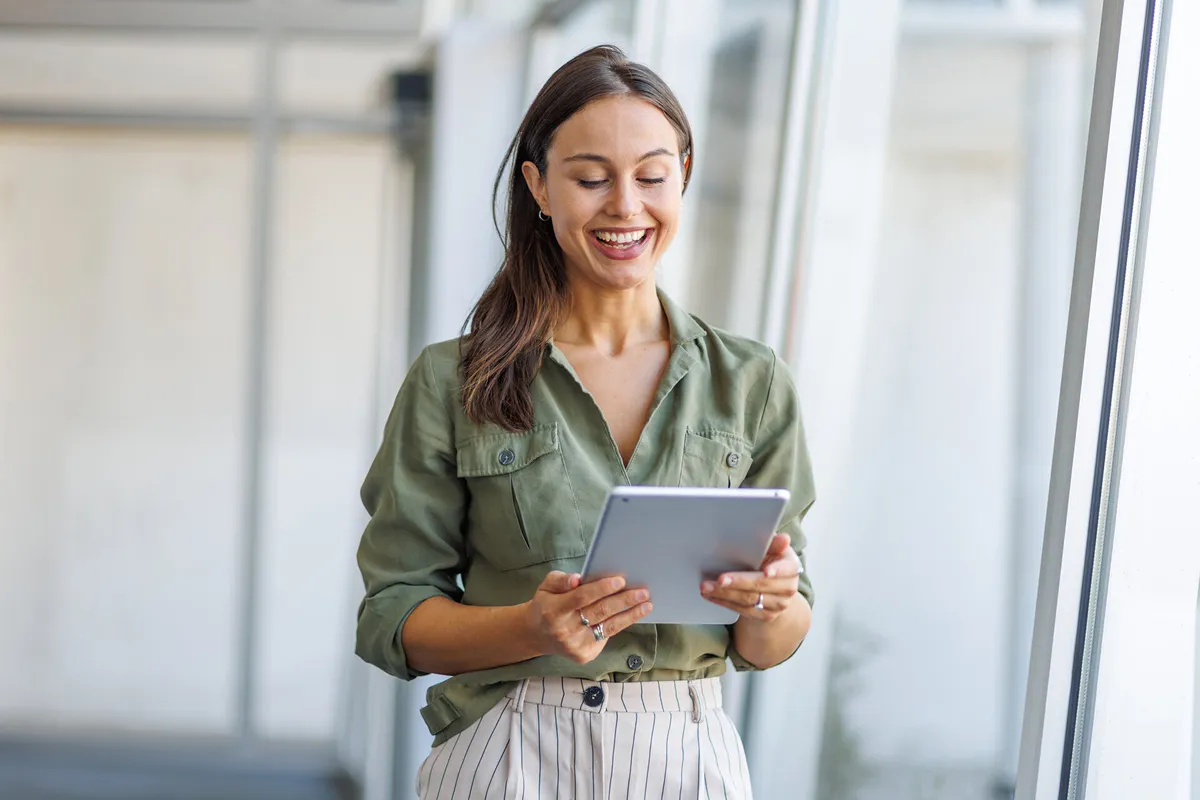 a smiling woman looking at a tablet and walking